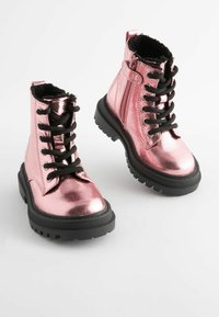 Bottines métalliques roses avec lacets noirs, doublure en fausse fourrure et semelle en caoutchouc noir texturée avec un motif de crampons épais.