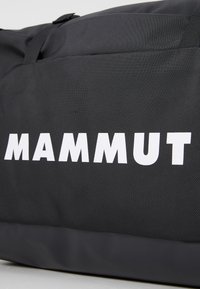 Black fabric duffel bag with a textured surface, featuring bold white "MAMMUT" branding on the side, sturdy carry handles, and a zip closure.