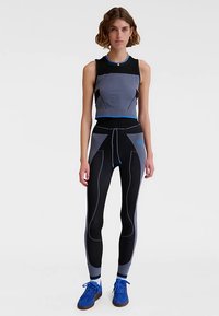 Sportowy strój składający się z dopasowanego szaro-czarnego crop topu z niebieskimi akcentami oraz czarnych legginsów z zakrzywionymi szarymi wzorami. Całość dopełniają niebieskie sneakersy.