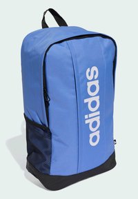 Mochila de tela azul con un gran logotipo blanco de "adidas", compartimentos con cremallera, bolsillo lateral de malla y base inferior negra. Correas de hombro ajustables.