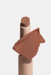 Fond de teint stick avec un échantillon de maquillage crème marron moyen sur un fond beige.