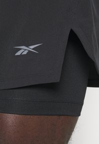 Černé sportovní šortky s světle šedým logem, vyrobené z lehkého materiálu, s těsnou vnitřní podšívkou a bočními rozparky pro vět�ší volnost pohybu.