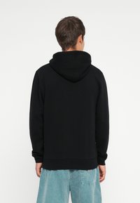 Black hooded sweatshirt with long sleeves and a ribbed hem, featuring a simple design. Worn with light blue denim shorts.