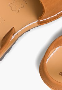 Skórzane sandały w kolorze brązowym o gładkim wykończeniu, z odkrytymi palcami i białymi szwami. Posiadają miękkie, zaokrąglone krawędzie oraz teksturowaną wkładkę.