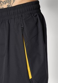 Sorte atletiske shorts med elastyse talje, der har en sidelomme med lynlås omkranset af lys gul og strukturerede stofpaneler.