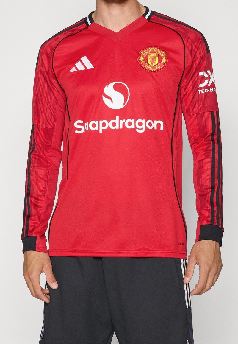 Maglia da football rossa a maniche lunghe in tessuto leggero. Presenta maniche a righe nere, un colletto a V e loghi degli sponsor sul davanti e sulle maniche.