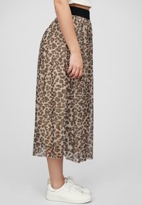 Průhledná, tan midi sukně s hnědým a černým leopardím vzorem. Má černý elastický pas. Nosená s bílými teniskami.