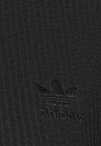 Czarna żebrowana tkanina z subtelną teksturą, z ciemnym wytłoczonym logo Adidas jako elementem identyfikacji marki.