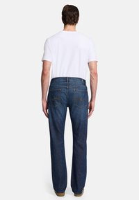 Blå denimjeans med rak passform, som har två bakfickor med sömnadsdetaljer och en hög midja. En enkel vit t-shirt bärs.