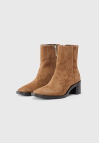 Stivaletti in suede marroni chiari con punta affusolata e tacco a blocco. Presentano una cerniera laterale e una texture liscia.