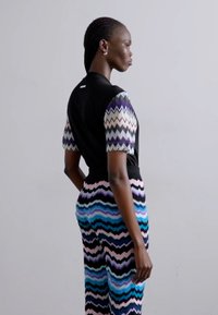 Μαύρη μπλούζα με κοντά μανίκια με σχέδιο ζιγκ-ζαγκ, σε συνδυασμό με παντελόνι σε πολλαπλά χρώματα με σχέδιο ζιγκ-ζαγκ που περιλαμβάνει αποχρώσεις του μπλε, ροζ και μαύρου.