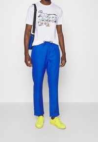 Bílý tričko s grafickým potiskem, modré kalhoty se šňůrkou a zářivě žluté tenisky. Tento outfit má uvolněný styl a pohodlný střih.