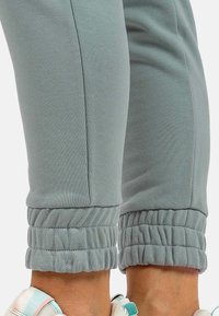 Lichtgrijze sweatpants hebben gerimpelde boorden, een gladde textuur en een aansluitend ontwerp, te zien van de middenkuit tot de enkel.