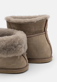 Brune semskede støvler med blødt, grått lammeskinnfôr. Lavskåret design med synlig søm langs kantene og en teksturert såle.