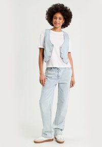 Veste en denim rayée bleu clair et pantalon assorti, avec un t-shirt blanc. La veste est dotée de boutons et d'une coupe décontractée. Des baskets décontractées complètent la tenue.
