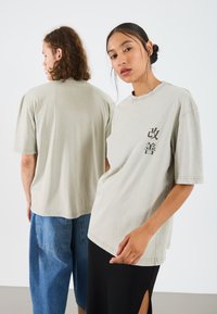 Hellgraues, übergroßes T-Shirt aus weichem Material mit einem in Schwarz bedruckten Design. Kurze Ärmel und runder Halsausschnitt.