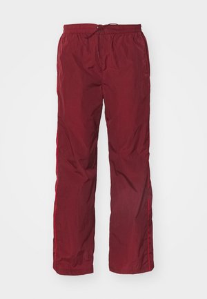 Pantalons d'extérieur légers et rouges avec une taille élastique et un cordon de serrage réglable. Comprend des accents en bande sur les côtés et une coupe ample et droite.