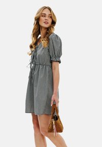 Čiernobiela kockovaná šaty s krátkymi naberanými rukávmi a sťahovacím pásom, skombinované s malou hnedou kabelkou.