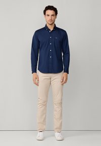 Chemise bleu marine à boutons, avec une poche poitrine, associée à un chino crème et des baskets blanches. Tissu lisse, coupe ajustée, sans motifs ni accents.