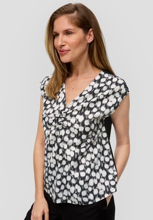 Zwart-witte blouse met korte mouwen en v-hals, met een textuur van stippen en een knoopdetail aan de voorkant. De gladde stof valt soepel.