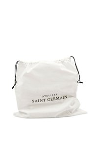 Witte katoenen trekkoordtas met zwarte letters "ATELIERS SAINT GERMAIN", met een zachte textuur en een iets gekreukelde vorm.