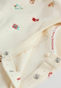 Crème-kleurige babyromper met feestelijke print van kerstbomen, cadeaus en vogels. Voorzien van drukknoopsluitingen en een geribbelde halslijn.