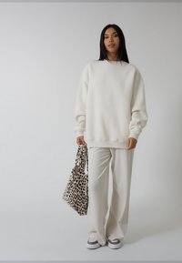 Balta pārmērīgi liela džemperis ar garām piedurknēm kopā ar baltām platām biksēm. Rokā tur leoparda raksta somu un valkā rakstainas slipona stila kurpes.