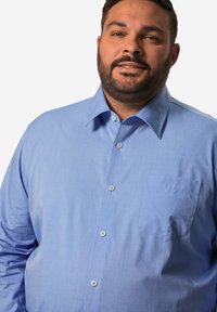 Lichtblauw overhemd met knopen en een zak, gemaakt van gladde stof. Heeft een klassieke kraag, subtiele textuur en ronde knopen.