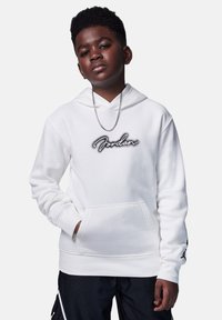Felpa bianca con cappuccio regolabile, dotata di un logo "Jordan" ricamato in nero sulla parte anteriore e di una tasca a marsupio. Indossata con pantaloncini neri.