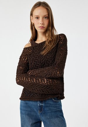Brun, stickad tröja med löst, öppet väv, off-shoulder design och långa ärmar, matchad med blå denimjeans.