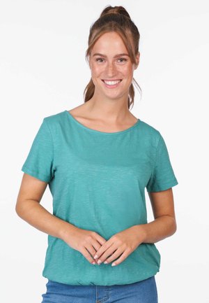 Türkises T-Shirt mit kurzen Ärmeln aus weichem Stoff, mit weitem Ausschnitt und relaxed Fit, kombiniert mit blauen Jeans.