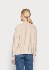 Beige sweater with a rounded neckline, dropped shoulders, and ribbed hem. Paired with high-waisted blue jeans. Soft texture.