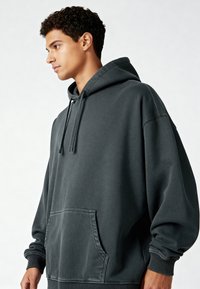 Felpa con cappuccio grigio scuro realizzata in tessuto morbido, con tasca frontale, cappuccio con coulisse e polsini a coste, dal design oversize.