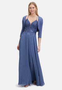 Długa wieczorowa sukienka w miękkim niebieskim materiale, z dopasowanym gorsetem ozdobionym misternymi koralikami i głębokim dekoltem, w zestawie z dopasowaną bolerko.