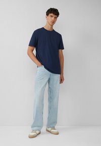 Granatowa bawełniana koszulka z krótkim rękawem, zestawiona z jasnoniebieskimi prostymi dżinsami i beżowymi sneakersami z białymi akcentami.