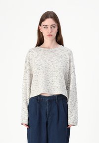 Maglione corto crema con un motivo testurizzato, maniche lunghe e scollo ampio, abbinato a pantaloni blu scuro a vita alta.