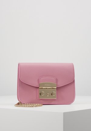 Sac bandoulière en cuir rose avec fermoir doré et bandoulière chaîne, présenté sur un piédestal blanc sur un fond gris clair uni.