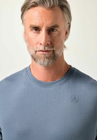 Niebieska bawełniana koszulka z okrągłym dekoltem i małym wytłoczonym logo na piersi. Gładka tekstura z luźnym krojem.