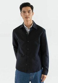 Svart knapp-up skjorte med et strukturert mønster, spredt krage og frontknapper, kombinert med blå denimjeans.