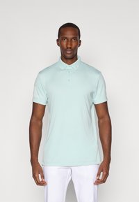 Mintgrønn polo skjorte med klassisk krage, korte ermer og et teksturert mønster på venstre erme. Jevn stoff, figursydd design.