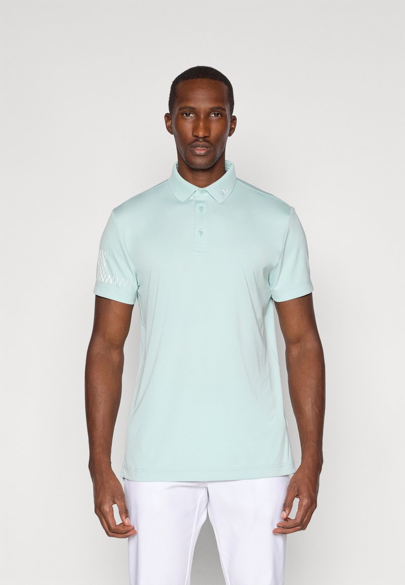 Mintgrønn polo skjorte med klassisk krage, korte ermer og et teksturert mønster på venstre erme. Jevn stoff, figursydd design.