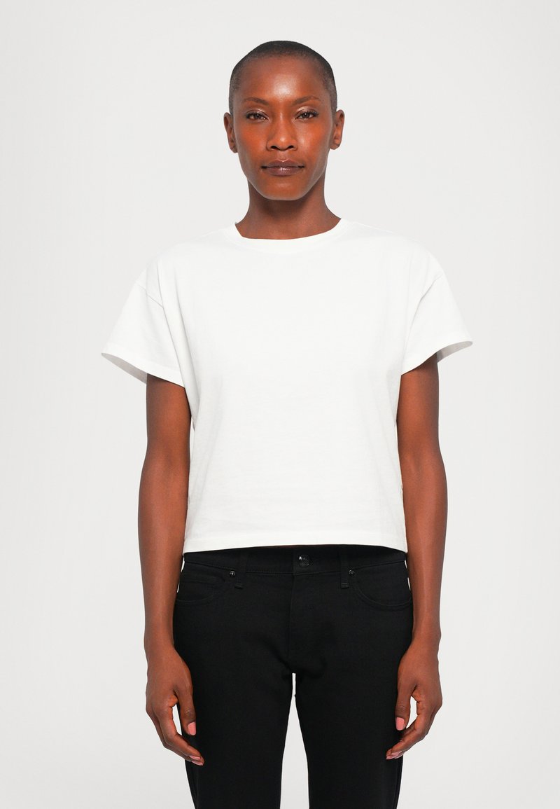 White cropped t-shirt with short sleeves, round neckline, made of smooth cotton fabric. Paired with black jeans. Minimalist design.