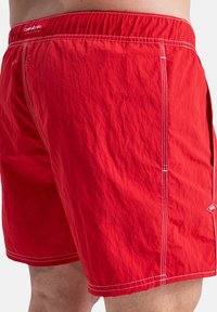 Red swim shorts made of lightweight fabric, featuring a textured surface, elastic waistband, and contrasting white stitching details.