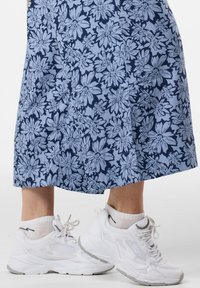 Vita sportskor i mesh och gummi, matchade med en lång blå blommig klänning med stora kontrasterande blommor.