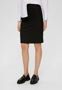 Zwarte kokerrok van gladde stof, met een aansluitend ontwerp en lengte tot de knie. Gecombineerd met glanzende zwarte loafers voor contrast.