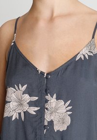Textured, dark gray sleeveless top with a V-neck, featuring light floral prints and button accents down the front.