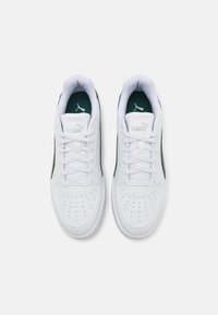 Hvide atletiske sneakers med perforeret tå, grønne detaljer, polstret krave og flade hvide snørebånd. Logo synligt på tungen og siden.