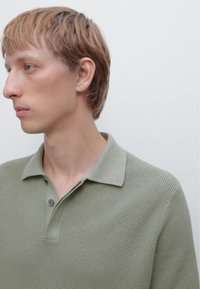 Polo shirt verde texturizzato con colletto, apertura con doppio bottone e maniche corte, che presenta un motivo a maglia sottile.