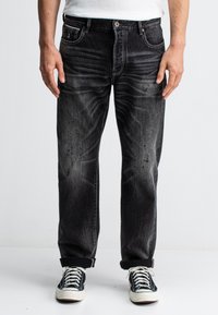 Schwarze Jeans mit einem verwaschenen Effekt, gerade Passform, Fünf-Taschen-Design und umgeschlagenem Saum, kombiniert mit schwarzen Sneakers mit weißen Schnürsenkeln.