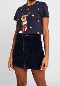 Marinblå bomullströja med en ren-klippning och gyllene stjärnor; ihop med en mörk kordflamskjol med blixtlås fram och strukturerad yta.